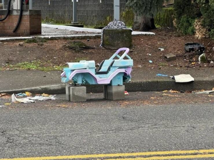 A pastel-colored toy car sits on concrete blocks on a street, with litter and debris scattered around.