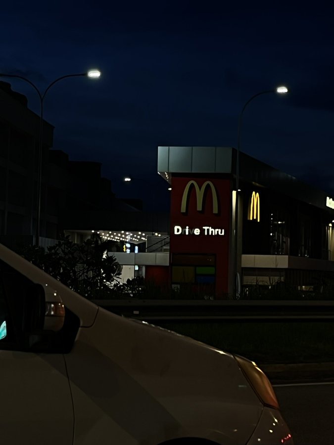 McDonald’s Drive Thru sign visible at night, with a white van in the foreground.