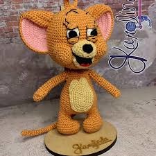Crochet mouse figurine with large pink ears, yellow body, and beige belly, standing on a wooden base.