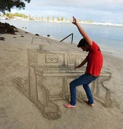 A man is playing a piano drawn in the sand on the beach.
