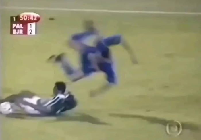 50:42 PAL 1 BJR 2. Un jugador de fútbol en uniforme azul está en el aire, mientras otro jugador en uniforme blanco y verde está en el suelo durante un partido.