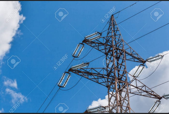 Una torre de transmisión de energía eléctrica contra un cielo azul con nubes.