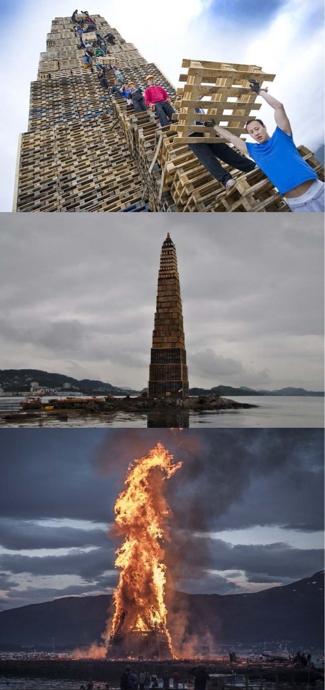 People building a giant tower out of wooden pallets, then the completed tower standing by the water, and finally the tower burning as a massive bonfire.