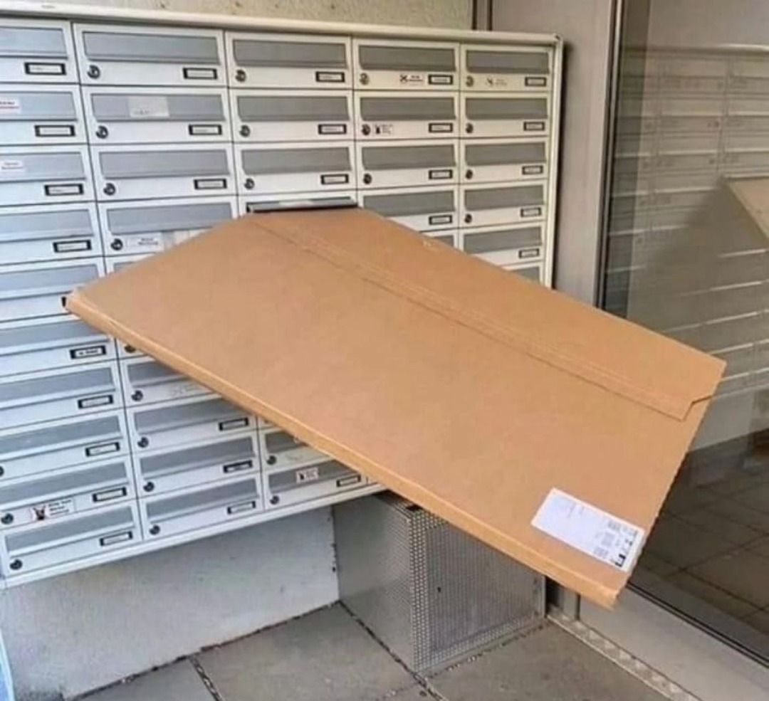 A large cardboard package is stuck in a small mailbox slot, clearly too big to fit, illustrating a delivery attempt gone wrong.