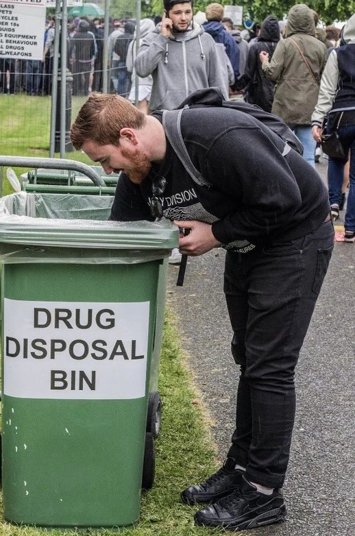 DRUG DISPOSAL BIN. A man is looking into a green bin labeled 'DRUG DISPOSAL BIN' at what appears to be a public event.