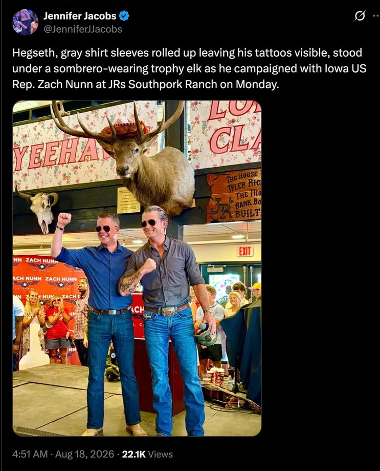 Hegseth, gray shirt sleeves rolled up leaving his tattoos visible, stood under a sombrero-wearing trophy elk as he campaigned with Iowa US Rep. Zach Nunn at JRs Southfork Ranch on Monday. Signs in the background read 'YEEHAW', 'THE HOUSE TYLER RIG & THE BIG BARK BO BUILT', and 'ZACH NUNN'. An 'EXIT' sign is also visible.
