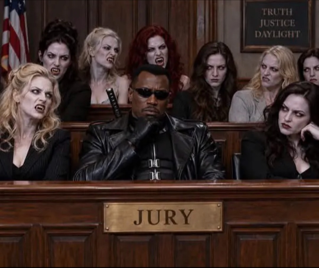 Blade sits in a jury box, looking stoic, while surrounded by several angry female vampires with bared fangs. A sign above reads 'TRUTH JUSTICE DAYLIGHT' and 'JURY' is visible on the box.